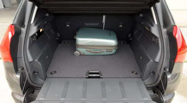 Otwarty bagażnik Peugeot 3008 z jednym zielonym walizką.