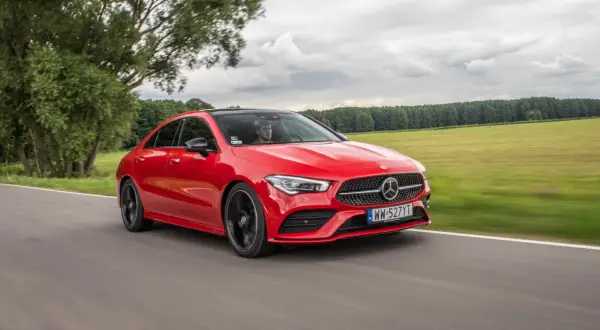 Czerwony Mercedes-Benz CLA Coupe pędzi po drodze wśród zielonych pól i drzew.