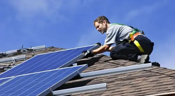 Installatore sul tetto, con imbracatura, che fissa pannelli fotovoltaici. L'orientamento dei pannelli è cruciale per massimizzare l'energia solare.
