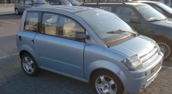 Niebieski, miejski samochód, który może być idealnym pierwszym autem od 16 lat. Stoi na parkingu obok innych pojazdów.