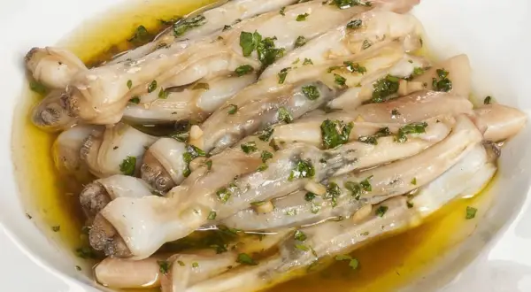Navajas a la plancha con ajo y perejil, servidas en un plato blanco con aceite dorado.