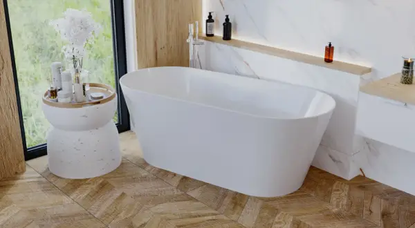 Elegancka wolnostojąca wanna w łazience z drewnianą podłogą ułożoną we wzór jodełki. Obok wanny stoi stolik z kosmetykami i kwiatami.