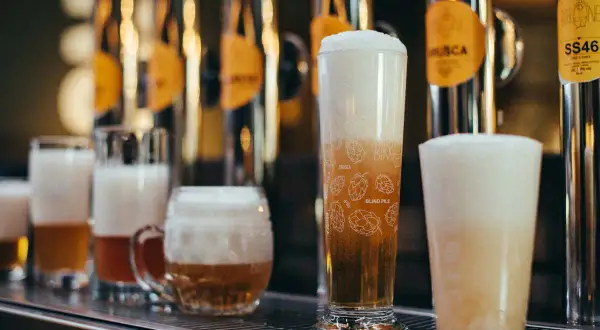 Bicchieri di birra con schiuma abbondante, tra cui una rye ipa decorata con luppoli.