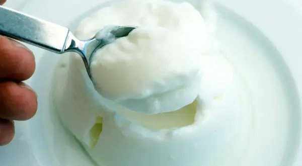 Cremiger Joghurt, eine köstliche Alternative zu saurer Sahne, wird mit einem Löffel aus einer Schüssel gehoben.
