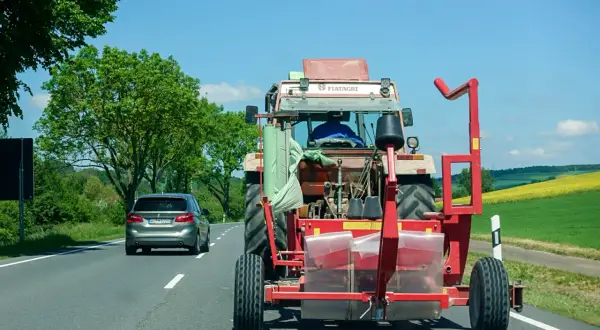 Ein Traktor mit Ballenwickler fährt langsam auf der Autobahn. Ein Auto dahinter gibt Lichthupe, um zu überholen.