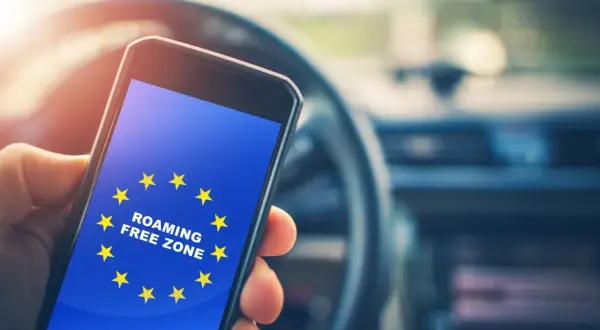 Dłoń trzyma smartfon z flagą UE i napisem "ROAMING FREE ZONE". Podróż po Europie bez dodatkowych opłat.