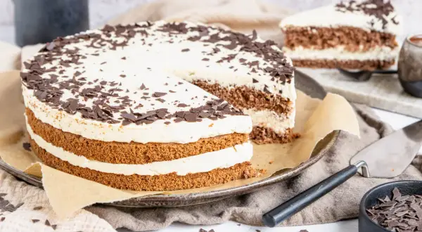 Eine köstliche Cappuccino Torte mit Schokoladenraspeln bestreut, auf einem Teller mit einem angeschnittenen Stück.
