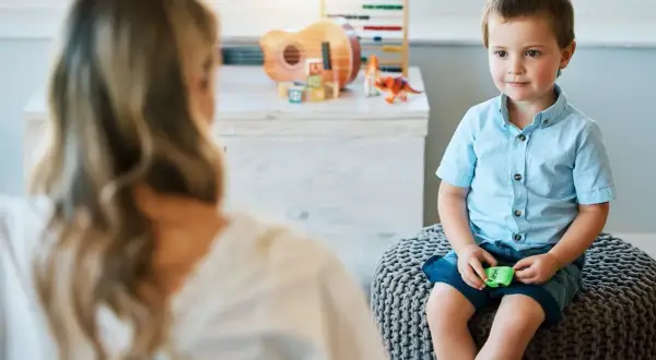 Chłopiec z afazją siedzi na pufie, rozmawiając z terapeutką. Czy dziecku z afazją przysługuje zasiłek pielęgnacyjny?