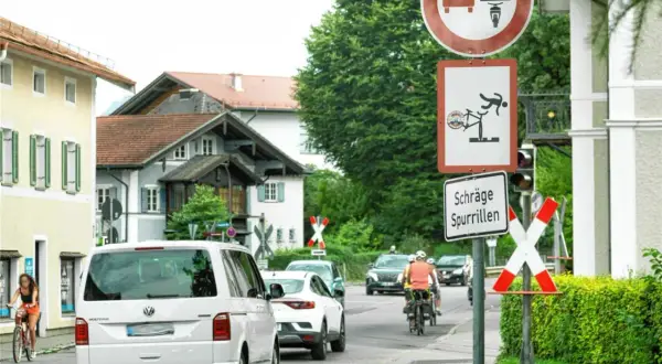 Verkehrszeichen 277 weist auf schräge Spurrillen hin. Ein Radfahrer wird gezeigt, der fast stürzt. Autos und Radfahrer fahren auf einer Straße.