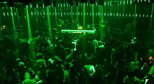 A crowded nightclub with green lights and a DJ booth.