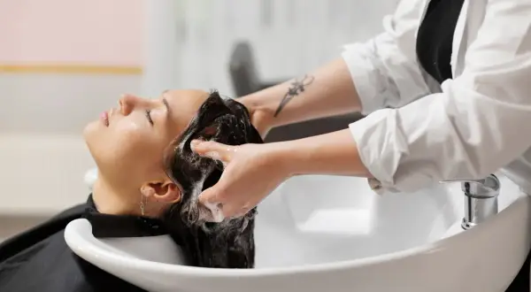Une coiffeuse masse le cuir chevelu d'une cliente, créant une mousse onctueuse. Un moment de détente pour des cheveux sans sulfate.