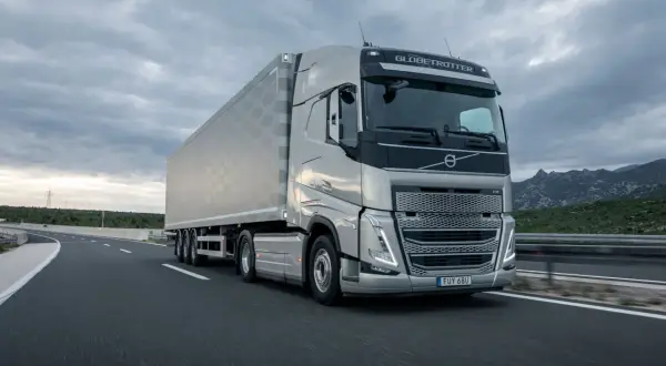 Un tracteur Volvo FH Globetrotter tracte une semi-remorque sur une autoroute. La longueur impressionnante de l'ensemble est mise en valeur par le paysage montagneux en arrière-plan.