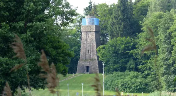 Kamienna wieża Bismarcka w Szczecinku, otoczona zielenią, z błękitnym elementem na szczycie.