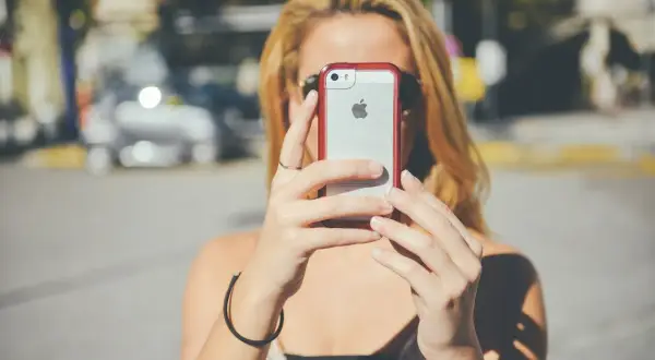 Kobieta z blond włosami trzyma iPhone'a, być może wykonując twardy reset.