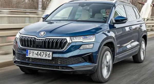Niebieski Skoda Karoq w ruchu, z kierowcą za kierownicą. Sprawdź aktualną skoda karoq cena.