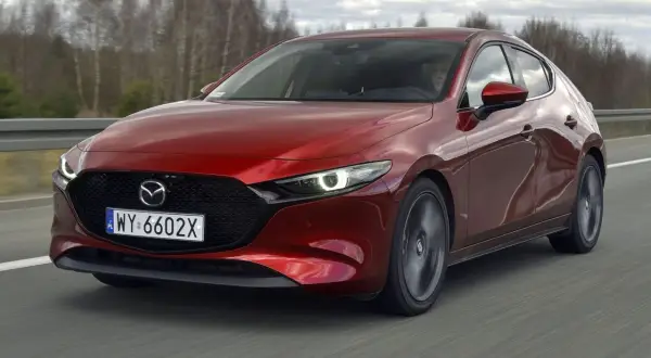 Czerwona Mazda 3 2.0 150KM w ruchu. Kierowca za kierownicą, dynamiczna jazda po drodze.