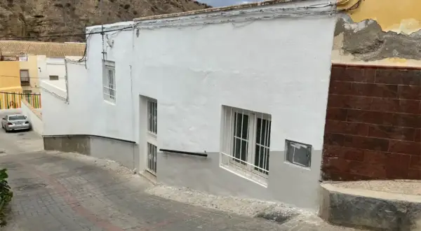 Calle empedrada en un pueblo blanco de Andalucía, con casas encaladas y una ladera rocosa al fondo. Un coche plateado aparcado. Gador, Almería.