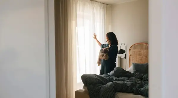 En kvinna med en sovande bebis i famnen står vid fönstret, kanske för att få lite lugn från baby blues.