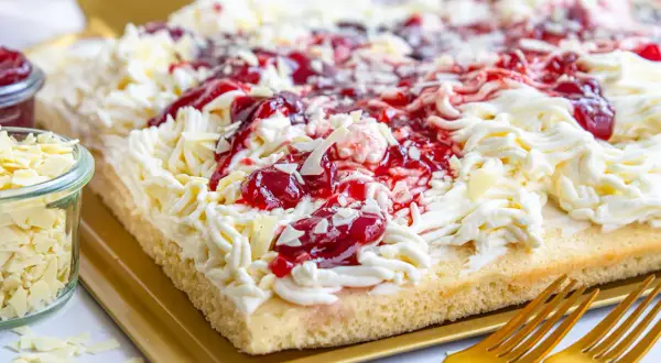 Ein köstlicher Spaghetti-Kuchen vom Blech, verziert mit Sahne, Kirschen und weißen Schokostreuseln.