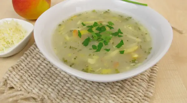 Aromaticzna zupa chrzanowa z chrzanem ze słoika, udekorowana natką pietruszki, obok jabłko i starty ser.
