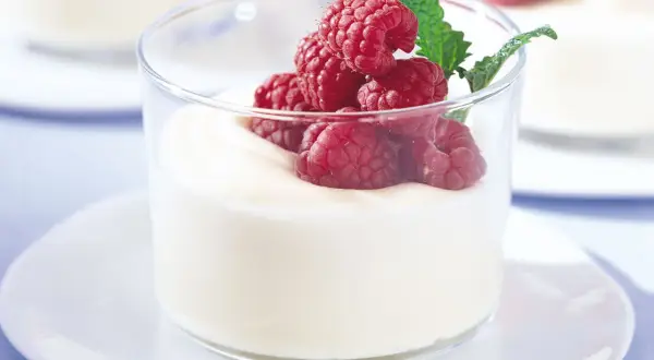 En len vit chokladmousse toppas med färska hallon och en myntakvist i ett glas.