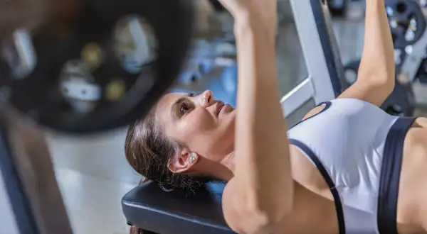 Kvinna utför incline press med skivstång på ett gym.