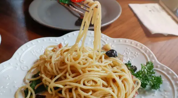 Widok z bliska na talerz pysznego spaghetti aglio olio, z widelcem unoszącym porcję makaronu, listkami bazylii i pomidorkiem.