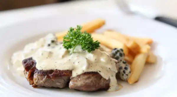 Filete de res bañado en cremosa salsa a la pimienta, acompañado de papas fritas y perejil fresco.