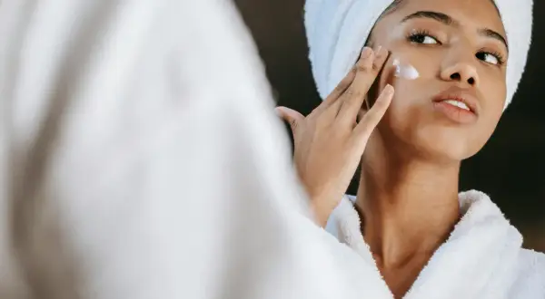Frau mit Handtuch auf dem Kopf trägt Creme auf, die Glykolsäure und Niacinamid enthält.