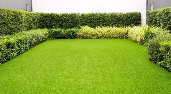 Un jardín impecable con césped artificial verde vibrante, rodeado de setos y plantas. Ideal para quienes buscan cual es el mejor césped artificial para jardín.