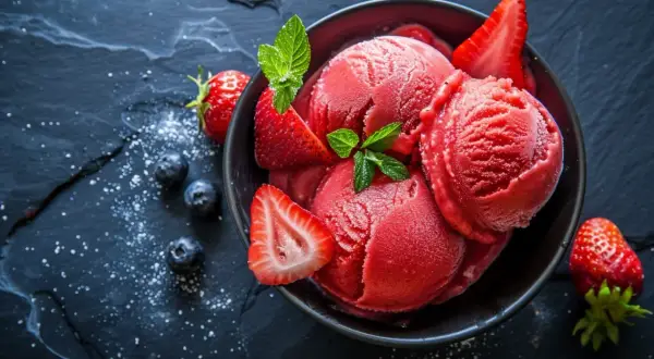 Schüssel mit fruchtigem Erdbeer-Eis aus Saft, frisch aus der Eismaschine, garniert mit Erdbeerscheiben und Minze.