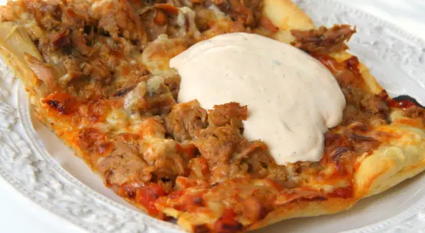 En bit pizza med tonfisk och fetaost, toppad med en krämig sås.