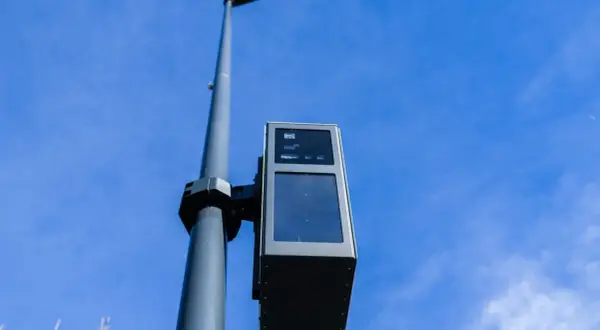 Un radar de ceinture, fixé sur un poteau, surveille la route sous un ciel bleu.