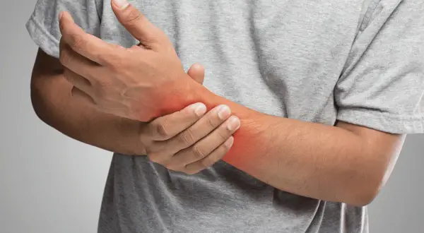 Uomo con dolore al polso, evidenziato da un'area rossa. Potrebbe indicare una distorsione al polso o un'altra infiammazione.
