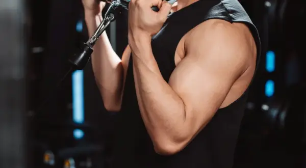 Mięśnie bicepsa mężczyzny ćwiczącego na siłowni. Cytrulina co daje? Poprawia przepływ krwi, co może wspierać trening.