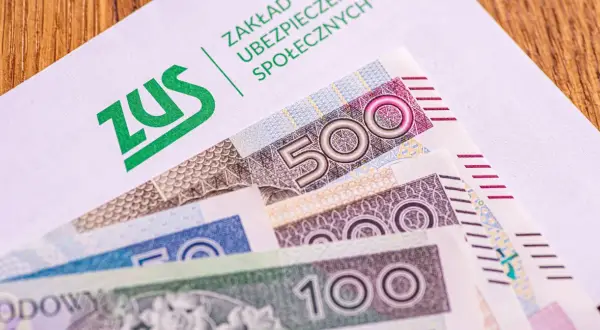 ZUS na białej kopercie, pod nią polskie banknoty 500, 200 i 100 zł. Czekamy na 14. emeryturę.