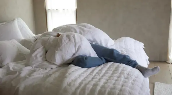 A person sleeps under white linen sheets, a cozy scene that hints at how to wash linen sheets for ultimate comfort.