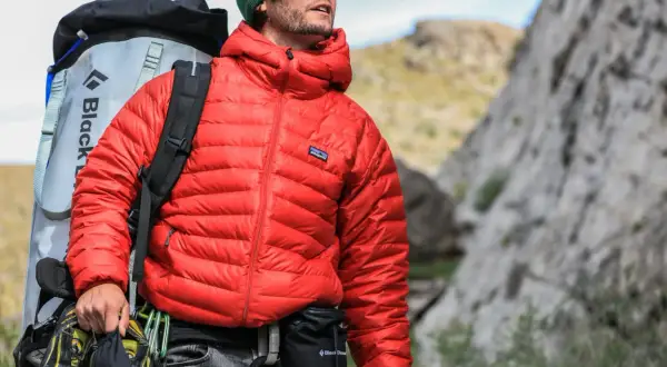 Escaladeur portant une veste rouge en matière doudoune, sac à dos et chaussures d'escalade.