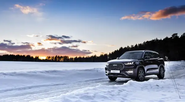 Un SUV noir roule sur une route enneigée au coucher du soleil. La loi montagne impose des équipements pour affronter ces conditions.