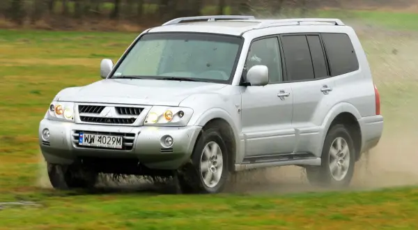 Srebrny Mitsubishi Pajero 3 pokonuje błotniste rozlewiska, unosząc chmury kurzu i wody.