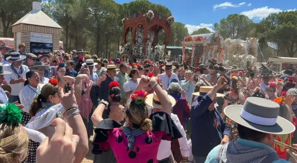 Multitud celebra con alegría, bailando y cantando al paso de una carreta adornada. Se percibe el espíritu de una sevillana rociera en pleno fervor.