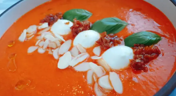 Aksamitna zupa z pieczonej papryki, ozdobiona kulkami mozzarelli, suszonymi pomidorami, płatkami migdałów i listkami bazylii.
