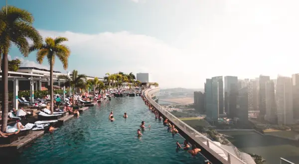 Menschen entspannen sich in einem Infinity-Pool mit Blick auf die Skyline von Singapur. Die **Singapur Regeln** für den Pool sind klar: Genießen!