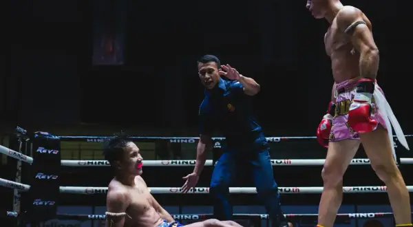 Domare stoppar en match i muy thai. En fighter ligger på mattan, den andra står redo.