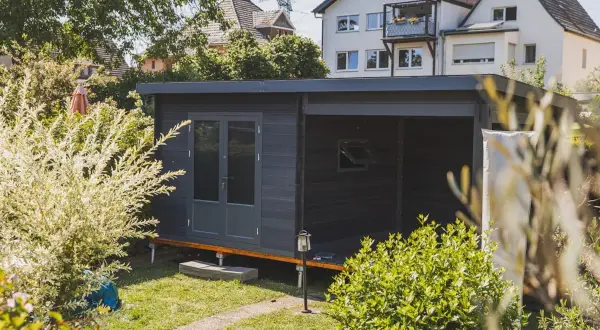 Modernes Gartenhaus mit Doppeltür und überdachter Veranda, ideal als Teil einer bauanleitung gartenhaus. Umgeben von üppigem Grün.