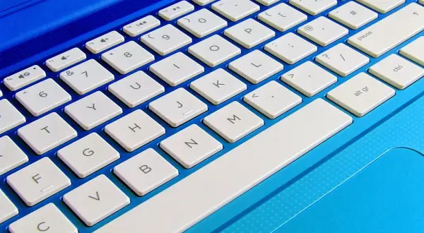 Niebieski laptop z białymi klawiszami. Dowiedz się, jak podłączyć klawiaturę do laptopa, aby ułatwić sobie pisanie.