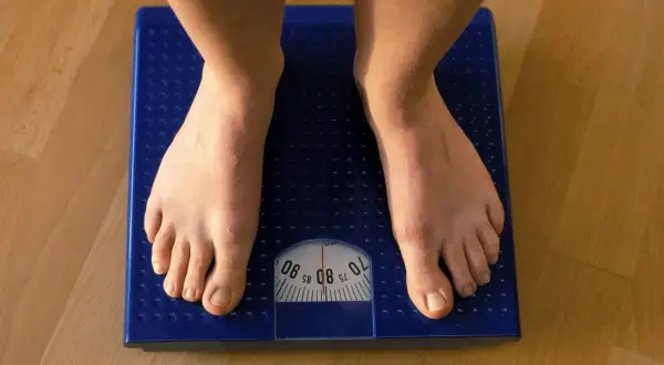 Füße auf einer blauen Waage. Die Anzeige zeigt etwa 80 kg. Muskeln sind schwerer als Fett, aber die Waage zählt beides.