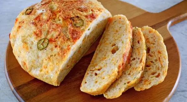 Chleb z serem i papryczką jalapeno, pokrojony na kromki, leży na drewnianej desce.