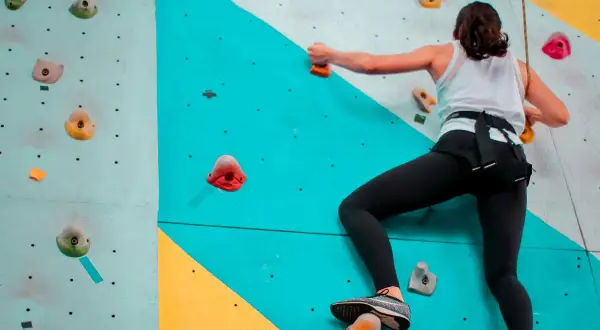 Une femme en tenue de sport fait de l'escalade sur un mur coloré, cherchant la prochaine prise.