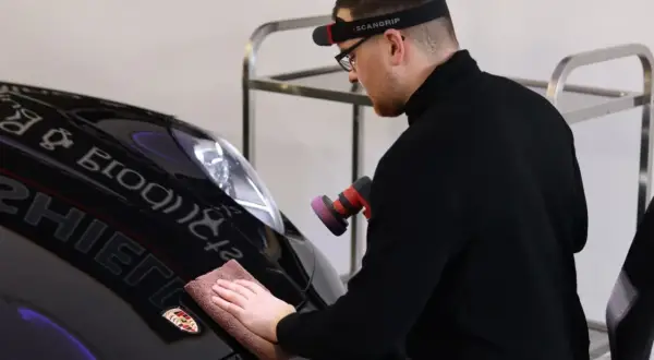 Man polerar en svart Porsche efter lackering med en polermaskin och mikrofiberduk.